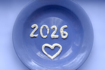 Dairy products in new year. Numbers 2026 and heart made of cream on blue plate.