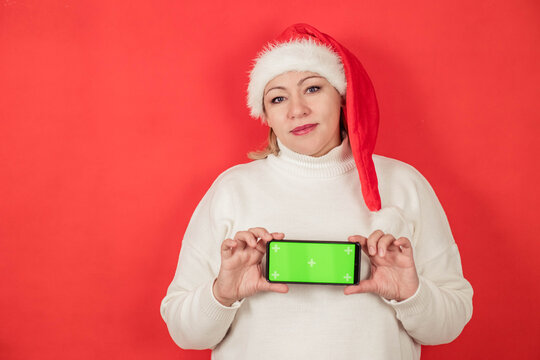 Plus Size Woman In Santa Hat On Red Background, Holding In Hands In Green Screen Smartphone, Copy Space, Chroma Key