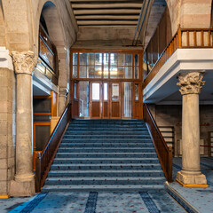 Interior of Kayseri Grand Mosque, Ulu Camii, Kayseri, Turkey. Features a blue carpeted staircase with wooden railings, stone columns, and a wooden entrance.