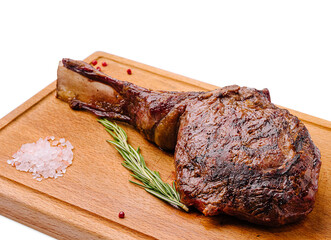 Cooked ribeye steak on wooden cutting board with rosemary and salt