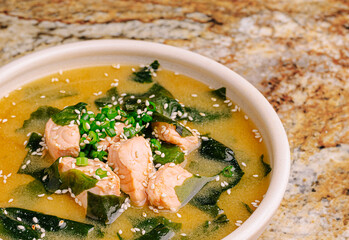 Delicious bowl of seaweed soup with fish chunks and herbs on granite surface