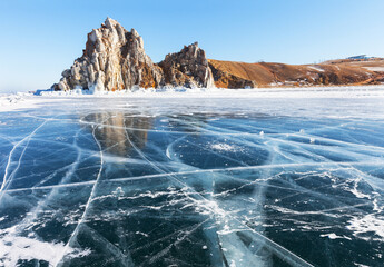 Winter Baikal Lake. View of famous Shamanka Rock or Cape Burkhan - natural landmark of Olkhon Island. Scenic winter landscape with blue clear ice with cracks on sunny February day. Nature background