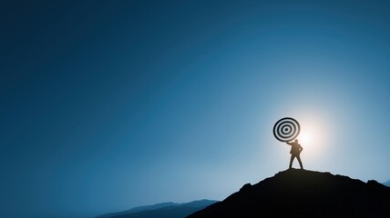 Silhouette of a businessman holding target board while standing on the top of mountain