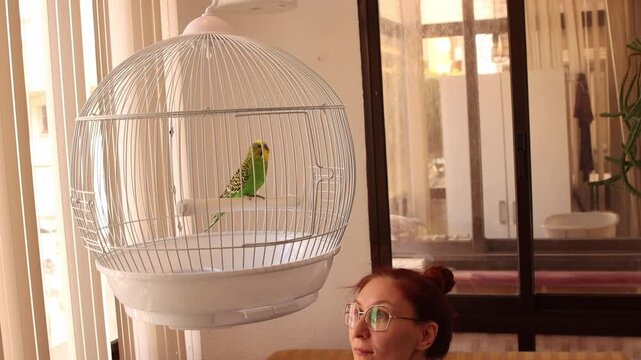 Mother and son interacting with pet bird in a cage at home