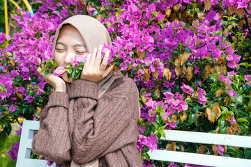 A Muslim Asian woman appears graceful and peaceful as she poses for a photo, kissing a lush purple...