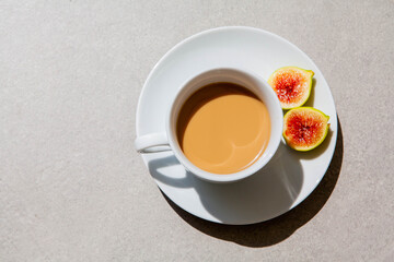 Warm cup of tea in a white ceramic mug with a fresh sliced fig on a saucer, placed on a textured stone surface in soft natural light, evoking calm, comfort, and slow living.