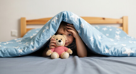 Young boy playing with teddy bear under blue blanket in bedroom  