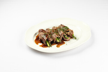 Tender roast beef slices wrapped around crisp asparagus spears and served with savory sauce on plate