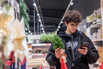 Teenager Shopping for Christmas Decor in Store While Comparing Prices on Smartphone &ndash; Modern Holiday Retail and Gen Z Consumer Behavior. Copyspace