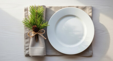 Simple white dishware with natural linen napkin. Pine branch and twine napkin ring as accent. Nordic style Christmas table setting, pine decor, neutral tones