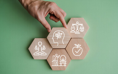 Hand placing a wooden hexagon with a brain icon among other health and wellness icons representing balance and holistic well being on a green background for a healthy lifestyle