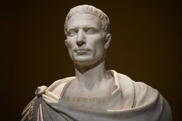 Close up portrait of a marble bust or statue of ancient Roman emperor Julius Caesar, standing in dark shadows