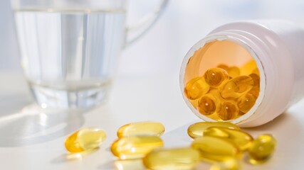 Bottle of fish oil capsules spilled next to a glass of water