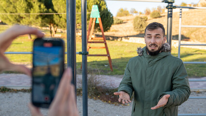 Content creator filming bearded man in a parka talking to a camera outdoors, making a video for digital platforms and followers