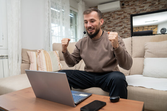 Young man celebrating success while working remotely or gaming at home, winning an online match