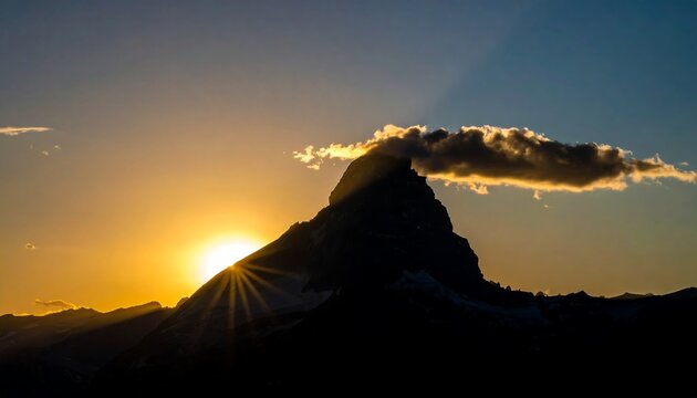 Majestic mountain silhouette against a vibrant golden sunset with partial cloud cover and striking light rays