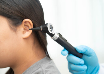 Otolaryngologist or ENT physician doctor examining senior patient ear with otoscope, hearing loss problem.