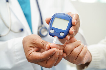 Asian doctor using digital glucose meter for check sample blood sugar level to treatment diabetes.