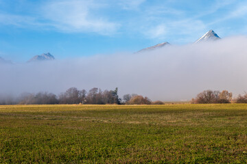 High Tatras peaks emerging from a thick inversion fog above fields and trees under a clear blue sky.
