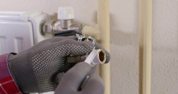 Installer wraps PTFE tape on male thread of fitting keeping tension even. Plumber rotates roll clockwise and covers thread crest leaving edge clean for seal