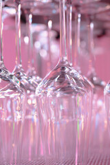 rows of clean upside-down wine glasses arranged on a shelf and illuminated with soft pink lighting. The reflective glass surface creates a modern, stylish atmosphere suitable for themes related to res