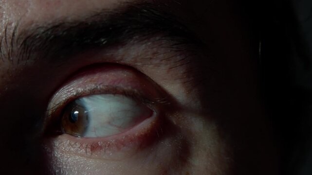 close brown eye caucasian male in macro sequence showing subtle eyelid movements, slow blinks and shifting gaze, clinical indoor lighting highlights skin texture and eyelash detail, slight redness