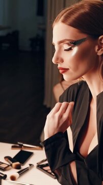 Model applies dramatic glitter eye makeup at vanity, palette and brushes on table, soft warm lighting, close-up profile with sculpted contour and glossy lips, poised expression evoking high-fashion