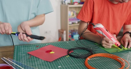 Girl recharges 3d pen with yellow filament while brother draws patterns at desk closeup. Schoolchildren learn to make models of hot plastic in school workshop - Powered by Adobe