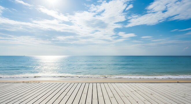 Sunlit ocean waves gently lap onto a weathered white wooden boardwalk under a vast blue sky with scattered clouds