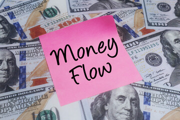 Pink sticky note with Money Flow text laid on a scattered background of US one hundred dollar bills, symbolizing financial movement and wealth circulation