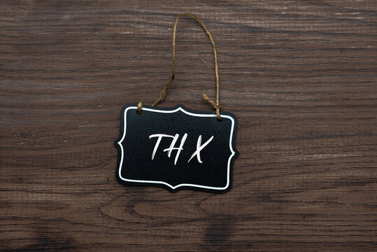 Hanging blackboard-style sign with the abbreviation "THX" in white script, displayed on a rustic wooden surface as a casual thank you.