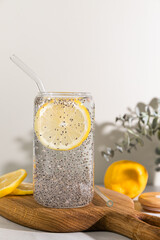 Refreshing lemon water with chia seeds in a clear glass with a glass straw on a wooden board in natural light.