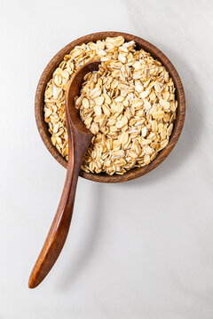Top view of rolled oats in a wooden bowl with a wooden spoon on a light background, healthy natural breakfast ingredient.
