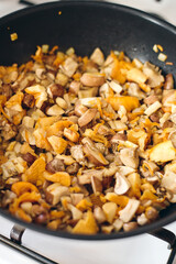 Finely chopped chanterelles, oyster mushrooms and champignons are fried in frying pan. Cooking process.