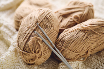 Crochet hooks and balls of beige and brown yarn on white knitted background. Knitting, crocheting supplies.