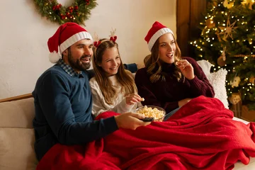Wandcirkels plexiglas Gekleurd Glas Happy family with daughter watching Christmas movie, eating popcorn while lying under blanket on sofa in living room with tree and glowing garlands  © Home-stock