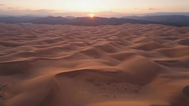 Aerial view of vast desert landscape with sand dunes and mountains at warm sunset light