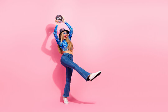 Glamorous young woman in blue print top jeans with disco ball against pink background maintains lively fashion lifestyle vibe and playful selfie style