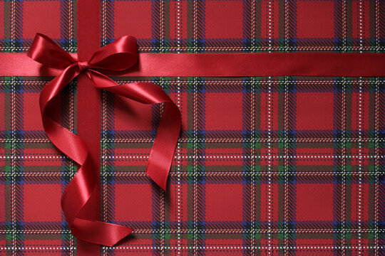 Christmas present, gift close-up. Red satin ribbon and bow on red, green and blue plaid paper background.