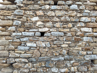 Weathered stone wall surface featuring small dark opening, showing rough layered rocks within soft daylight