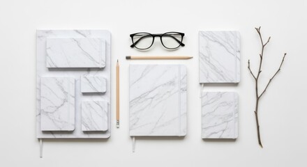 Elegant marble patterned stationery and reading glasses arranged artfully with a delicate branch on a white background