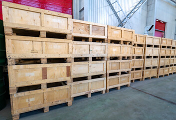 Rows of stacked wooden shipping crates and pallets inside a large warehouse or industrial storage facility.