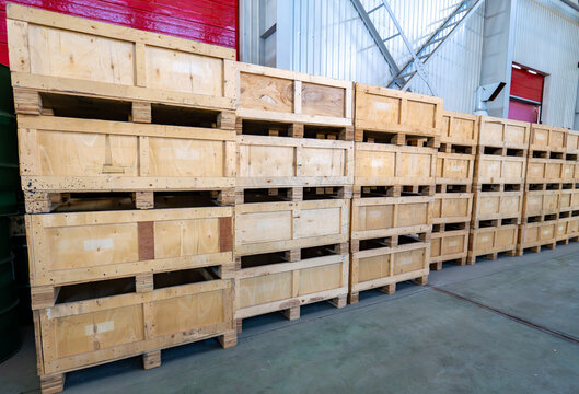 Rows of stacked wooden shipping crates and pallets inside a large warehouse or industrial storage facility.