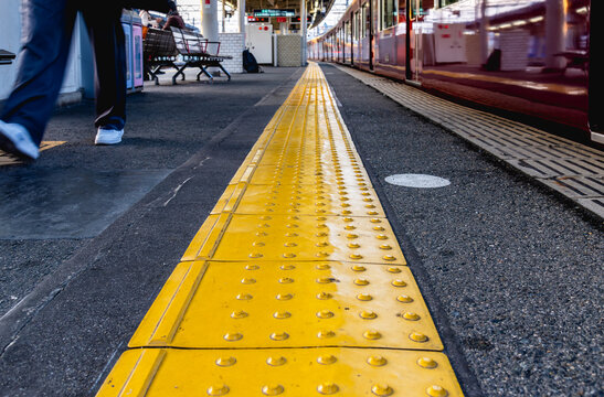 Yellow Braille block on a train platform at a Japanese railway station, designed for safety and accessibility for the visually impaired.