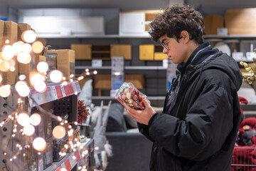 Teenager Choosing Christmas Ornaments in Store – Holiday Shopping, Festive Retail and Gen Z Consumer Behavior. Christmas Balls in Festive Store