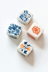 Four small, square, ceramic dice, decorated with floral motifs in blue and orange