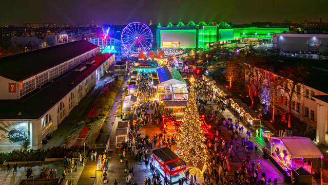 Night drone view of the Poznan MTP Christmas market with ferris wheel, Christmas tree and large festive crowds across the illuminated fairground