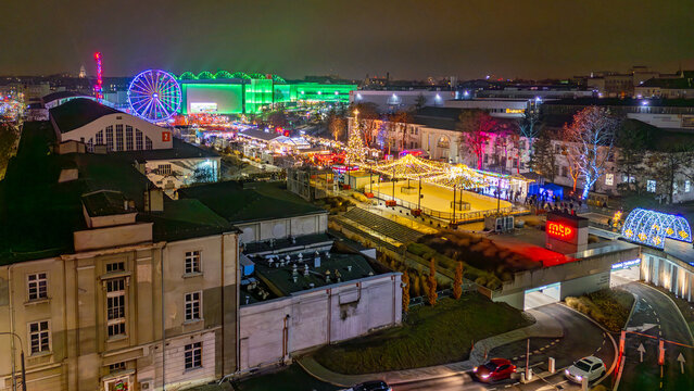 Night drone view of the Poznan MTP Christmas market with illuminated decorations, ferris wheel, ice rink and glowing festive fairground panorama