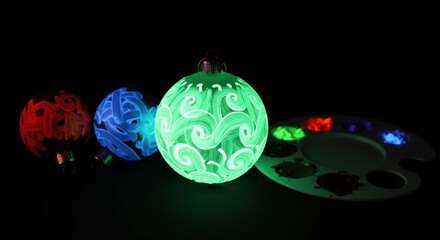 Hand-painted ornament glowing bright green in darkness. Regular ornaments and paint palette beside the glowing one.  Party Phosphorescent Paint, Glowing Ornaments in Dark Setting