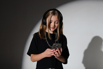 Fototapeta premium Young caucasian female teen using smartphone with headphones in studio lighting